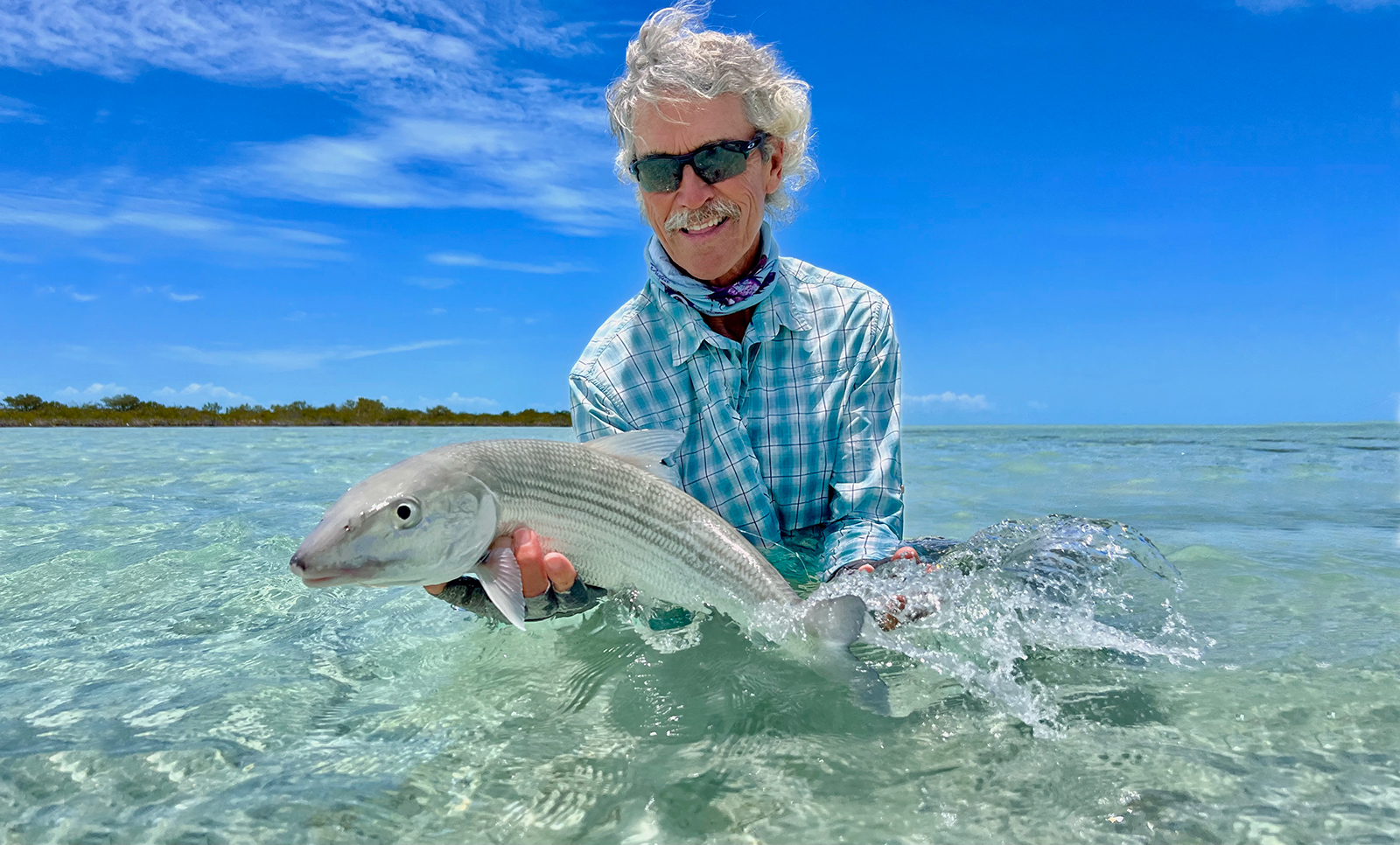 Fly fisherman wading the South Andros flats in the Bahamas with a bonefish catch at Mars Bay Bonefish Lodge.