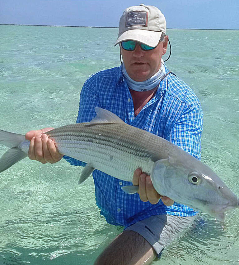 Angler holding a large bonefish in shallow turquoise water on South Andros.